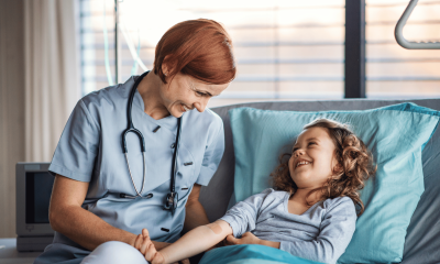 Nurse smiling down at happy young girl in hospital bed